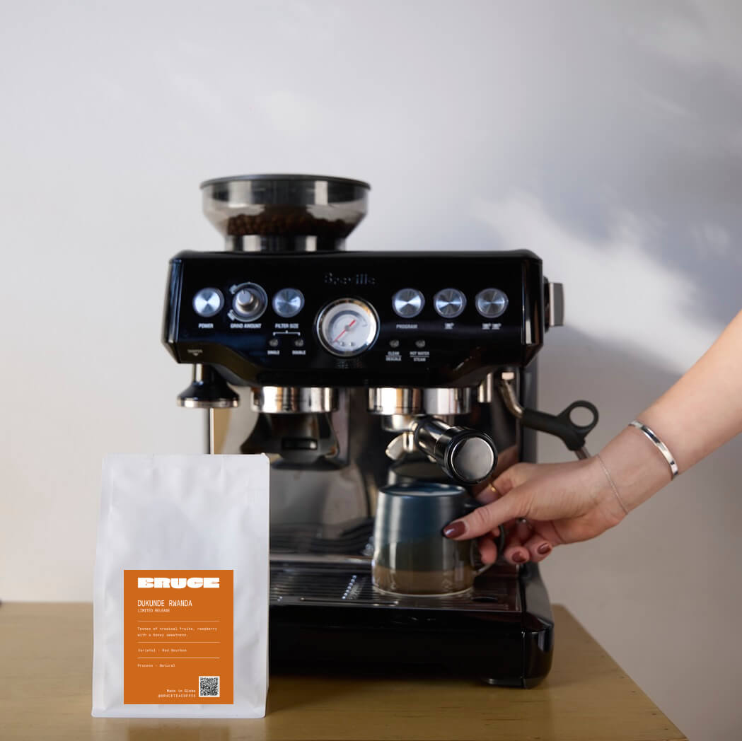 Dukunde red bourbon coffee beans next to Breville coffee machine on table