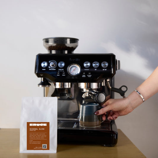 Bruce seasonal blend specialty coffee beans next to Breville Espresso coffee machine on a table.