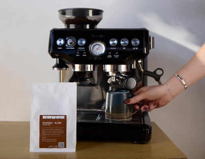 Bruce seasonal blend specialty coffee beans next to Breville Espresso coffee machine on a table.